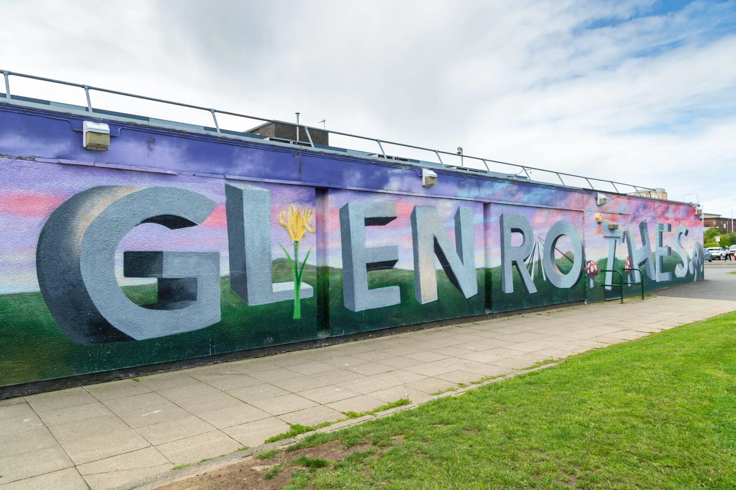 Mural art of "Glenrothes" in 3D-style letters with a flower and mushrooms on a landscape background.