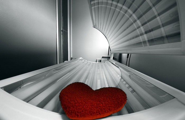 Red heart pillow inside empty tanning bed with doctors warning about diseases that should scare people more.