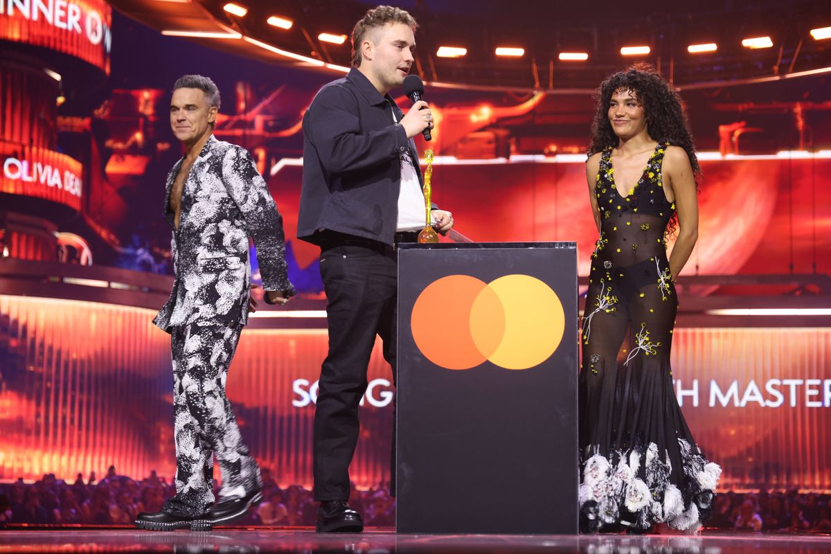 Sam Fender on stage accepting the 'Song of the Year' award with Olivia Dean and Robbie Williams 