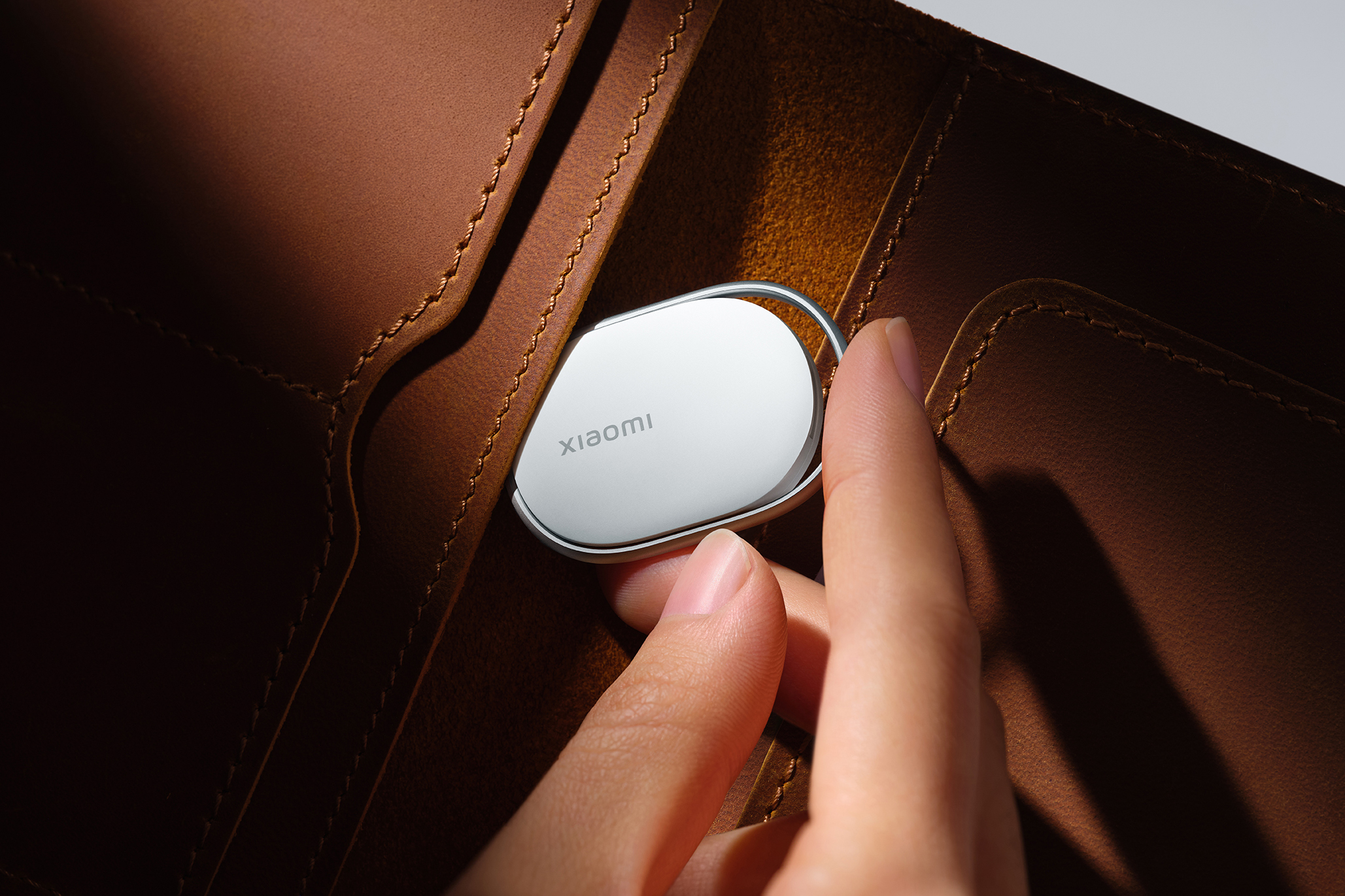 A person inserts the Xiaomi Tag tracker into the pocket of a wallet.