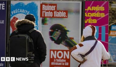 People in Geneva look at a poster urging people to vote "No" to funding cuts for the Swiss Broadcasting Corporation. Photo: February 2026