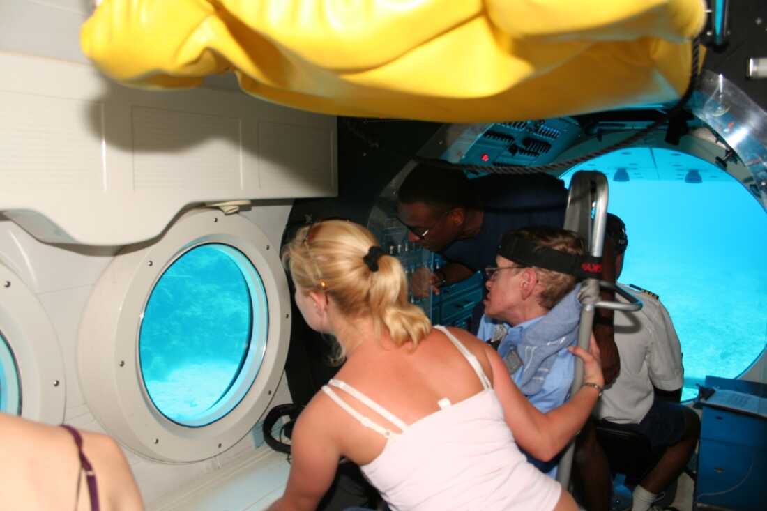 Stephen Hawking sits aboard a submarine in the U.S. Virgin Islands in March 2006. He's looking toward a circular porthole window, and on the other side is light blue water.