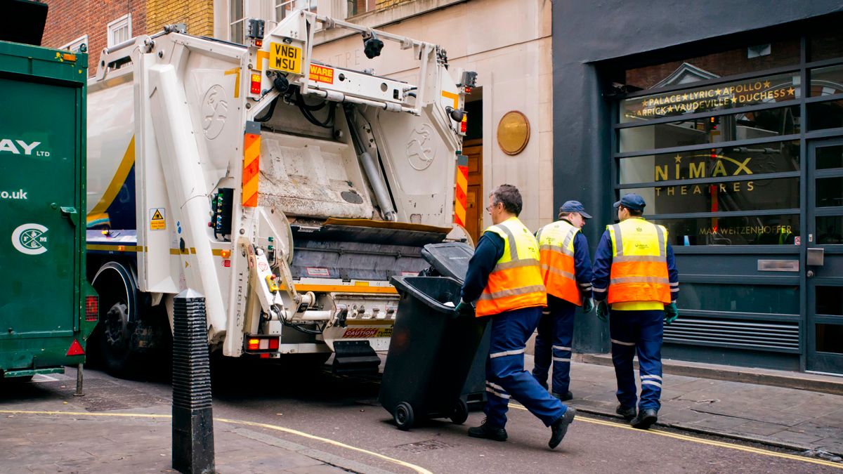 London, England - March 28, 2015: A crew of refuse collectors working in Maiden Lane in Central London, taking containers of rubbish to the lorry for loading. They are wearing bright yellow and orange hi-visability jackets to help them avoid accidental injury in London’s busy streets.
