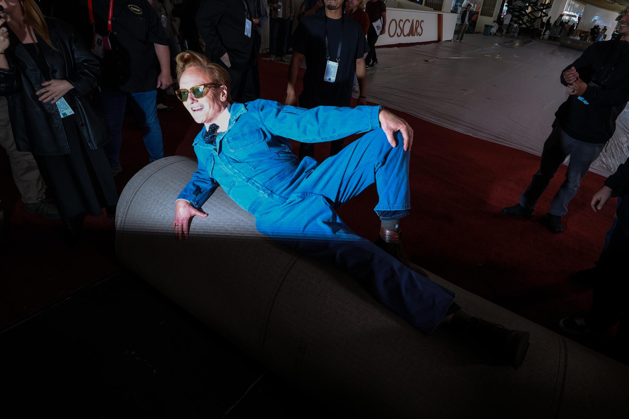 Conan O'Brien, wearing a denim jumpsuit, rolls out the red carpet.