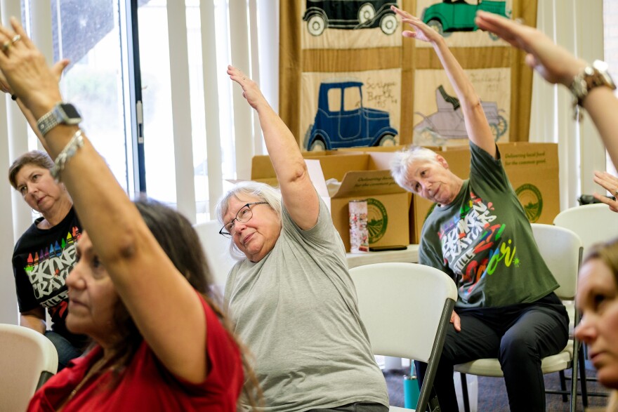 A photo of a group of seated women stretched with their left arms overhead. 