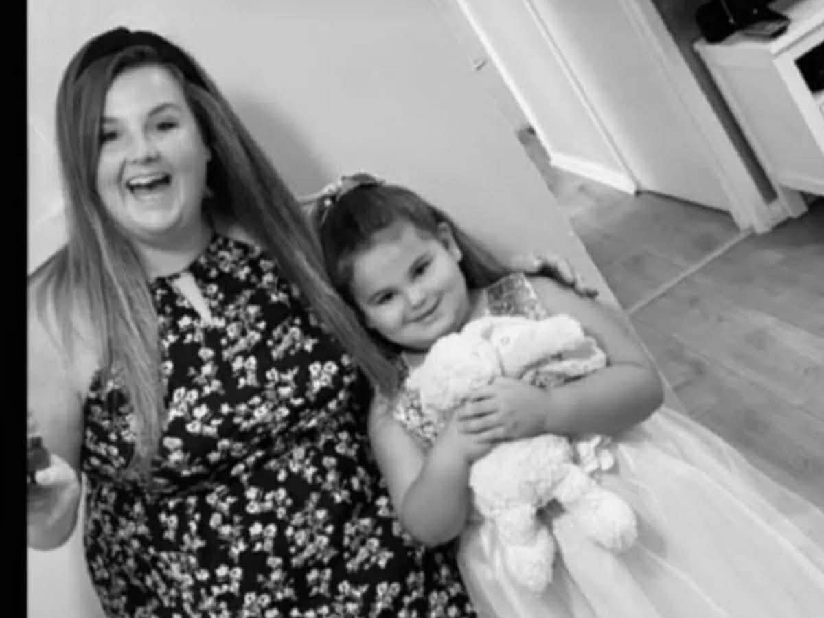 A black and white image depicts a woman standing next to a young girl, both of whom are smiling.