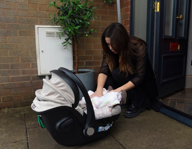 Carla Connor kneeling down to see to the baby in a car seat left at her doorstep in Coronation Street.