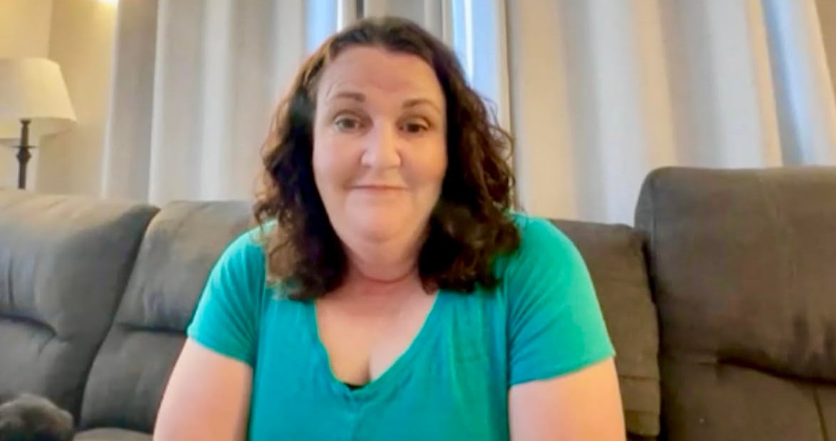 A woman with brown hair and a turquoise t-shirt looks at the camera while sitting on a couch