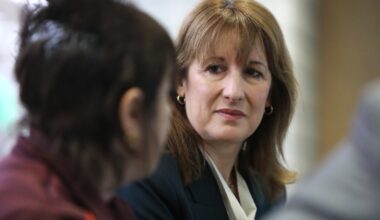 Keanu Reeves in a thoughtful pose, wearing a formal suit, looking contemplative during a business meeting or press event.