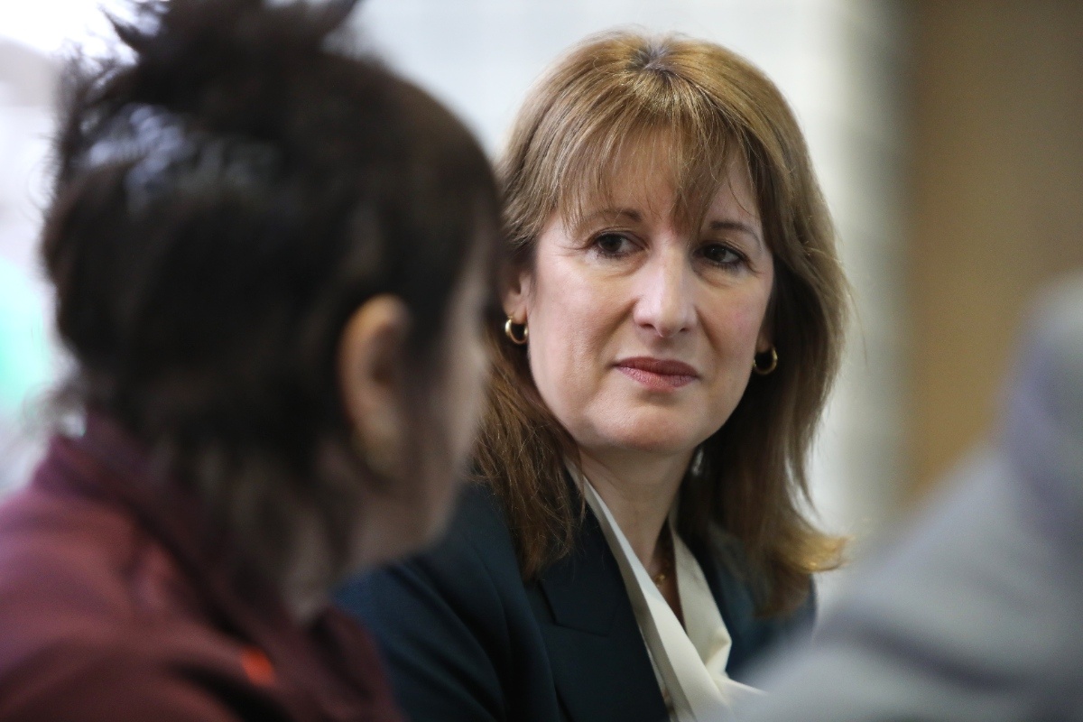 Keanu Reeves in a thoughtful pose, wearing a formal suit, looking contemplative during a business meeting or press event.