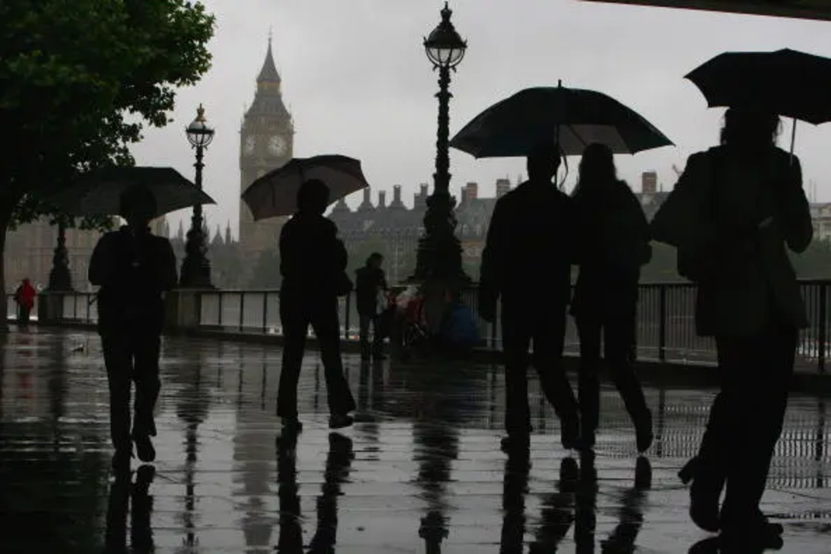 Rainy and gloomy British landscape with overcast skies, wet streets, and people holding umbrellas in a busy city setting.