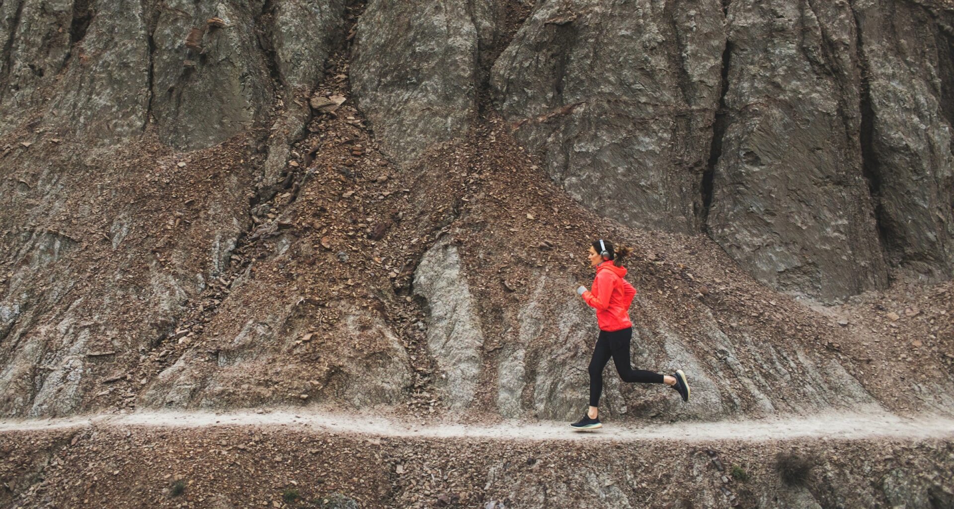woman running on rocky singltrack in red jacket
