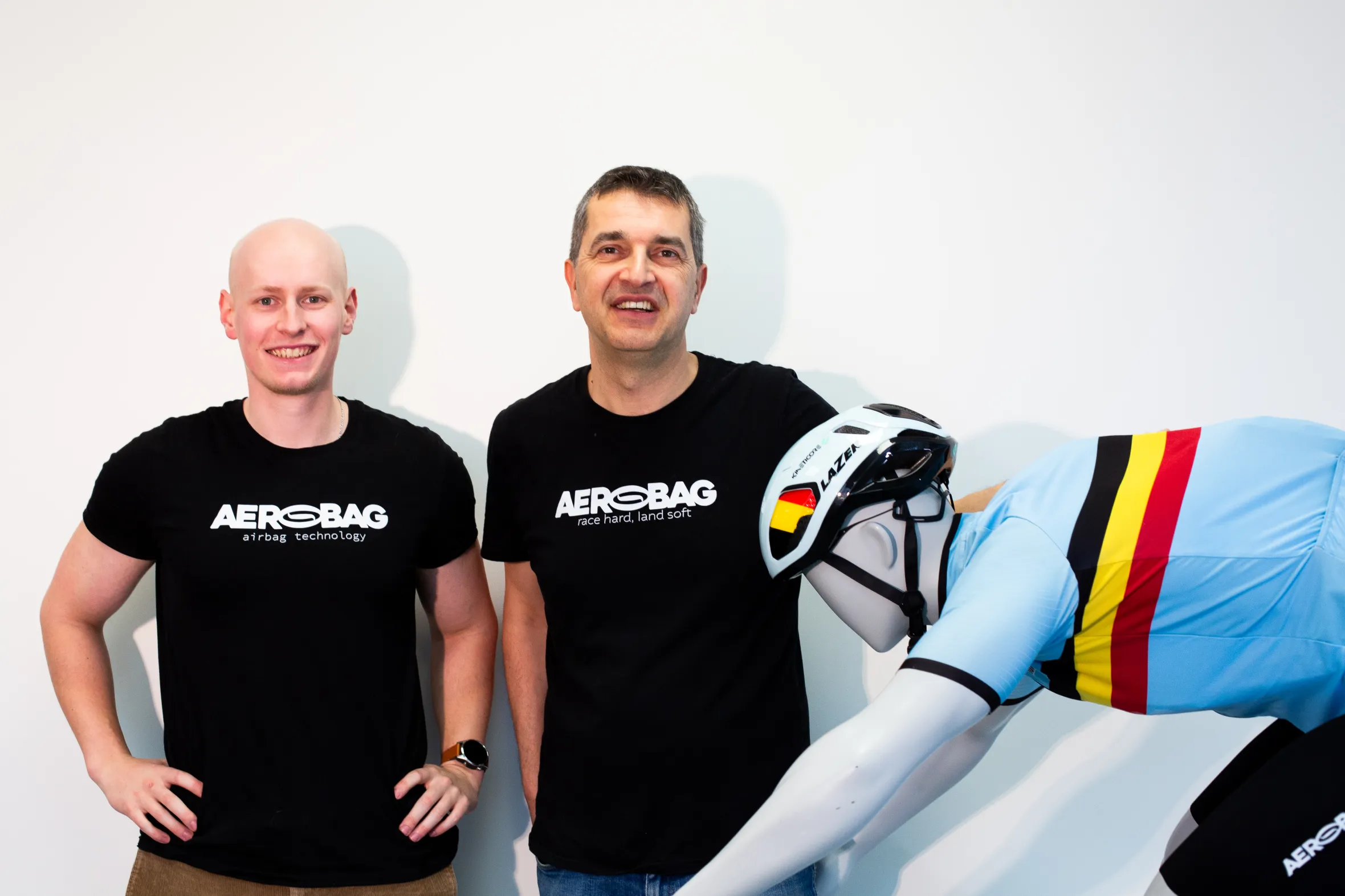 Two men in Aerobag shirts stand next to a mannequin wearing a cycling helmet and jersey.