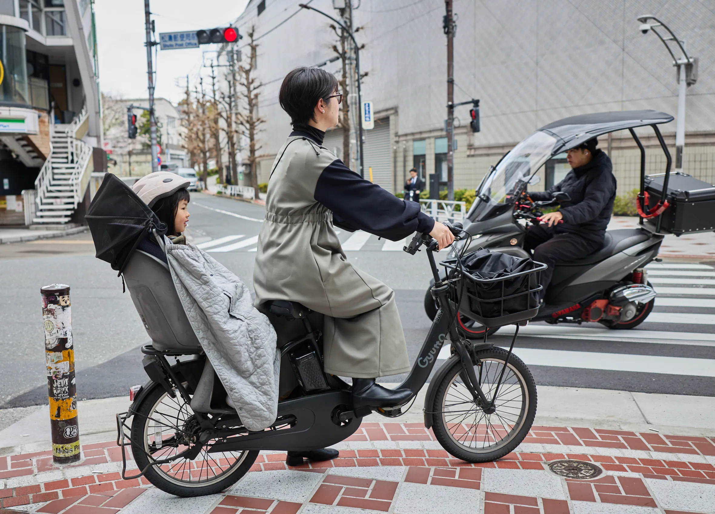 A Japanese mother and child on a bicycle with another person on a motor scooter in Tokyo, Japan.