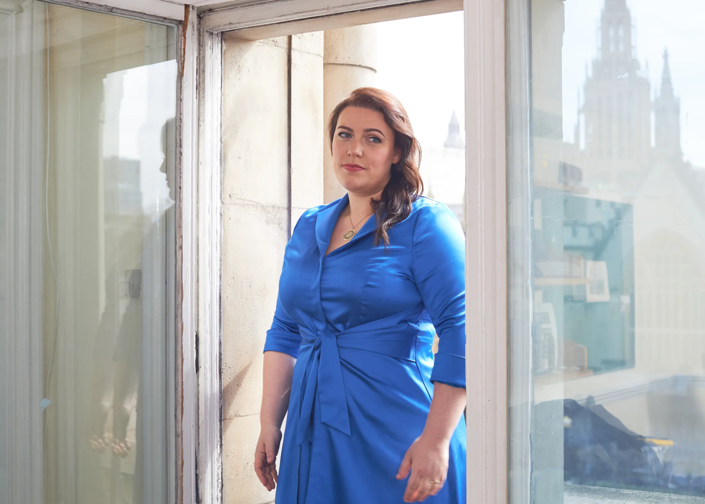 Alicia Kearns MP standing in a doorway wearing a blue dress.