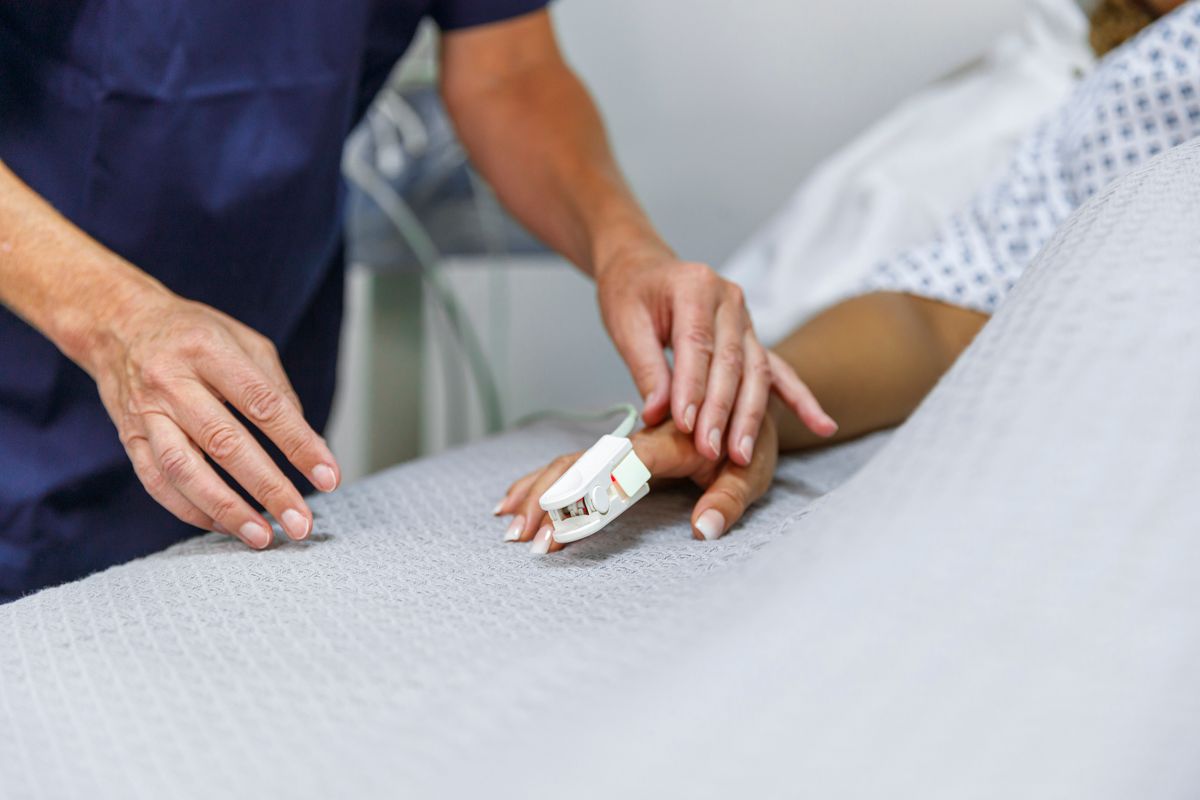 A close up of a nurse's hand putting a monitor on someone's finger