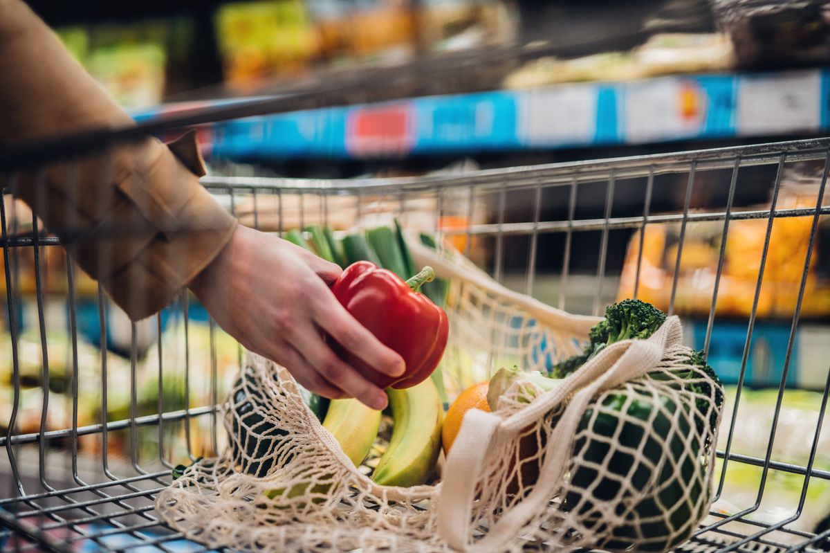 Close-up shot of female hand putting a red bell pepper into a mesh grocery bag. 