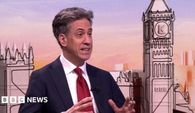 Energy Secretary Ed Miliband speaking on the Sunday with Laura Kuenssberg programme. He wears a dark navy suit, a white shirt and a ruby red satin tie.
