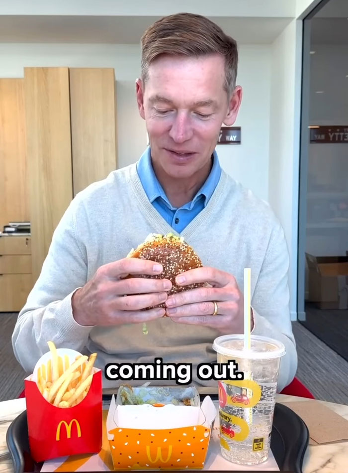Burger King boss holding a Whopper burger while sitting at a table with McDonald's fries and drink visible. Burger King boss holding a Whopper burger while sitting at a table with McDonald's fries and drink visible.