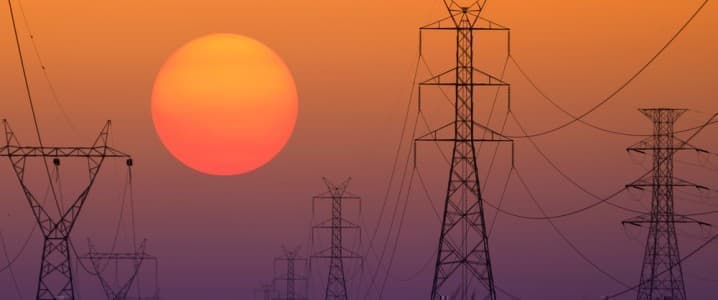 Power lines with a sunset behind in the distance.