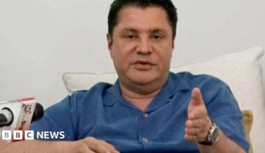 Rostam Aziz, wearing a blue shirt, speaking at a press conference