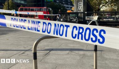 Blue and white police tape which reads 'police line do not cross'. A red London bus is in the background