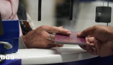 One hand is passing a red coloured passport to another over an airport desk.