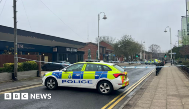 Image shows a police car blocking the road outside the Wall of Fame pub in Formby, Merseyside. There is also police tape across the road.