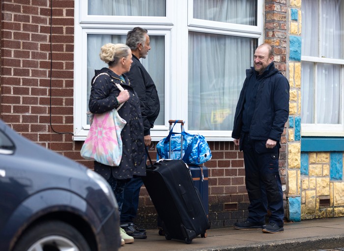 Mal talks to Bernie and Dev beside their suitcases in a scene from Coronation Street
