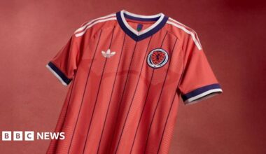 Salmon-pink Scotland shirt with dark purple pinstripes and white Adidas stripes down the shoulders and sleeves.