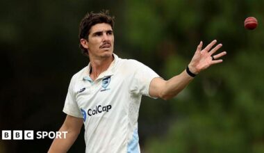 Sean Abbott extends his left arm to catch a red cricket ball, dressed in New South Wales' white kit