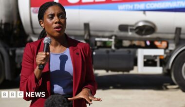 Badenoch speaks with a microphone in hand and gestures with the other hand while wearing a suit jacket and standing in front of a fuel tank truck with a Tory slogan on the side (the words 'with the Conservatives' are just legible in frame), in London last week.