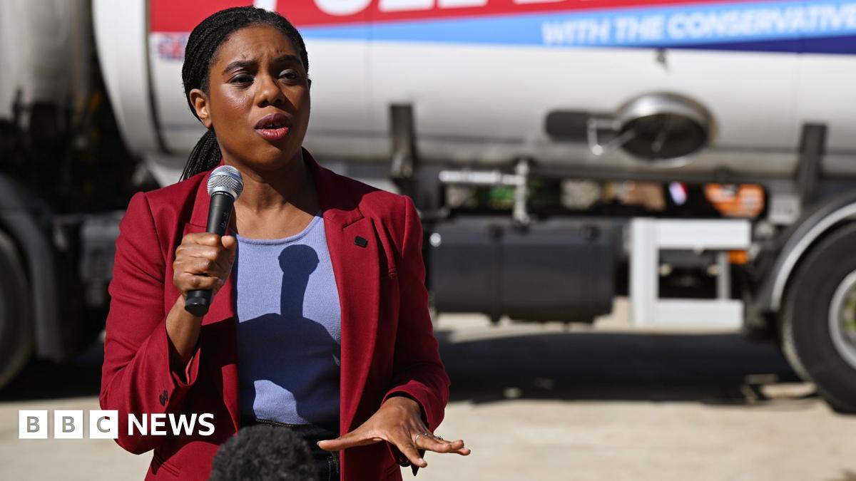 Badenoch speaks with a microphone in hand and gestures with the other hand while wearing a suit jacket and standing in front of a fuel tank truck with a Tory slogan on the side (the words 'with the Conservatives' are just legible in frame), in London last week.