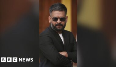 Man wearing black shades and a black blazer folds his arms.