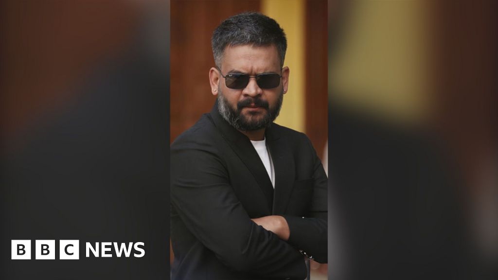 Man wearing black shades and a black blazer folds his arms.