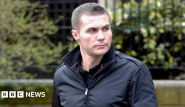 Steven Lyons has cropped brown hair and is wearing a black jacket with the collar turned up. He is looking off to the left with a serious expression on his face