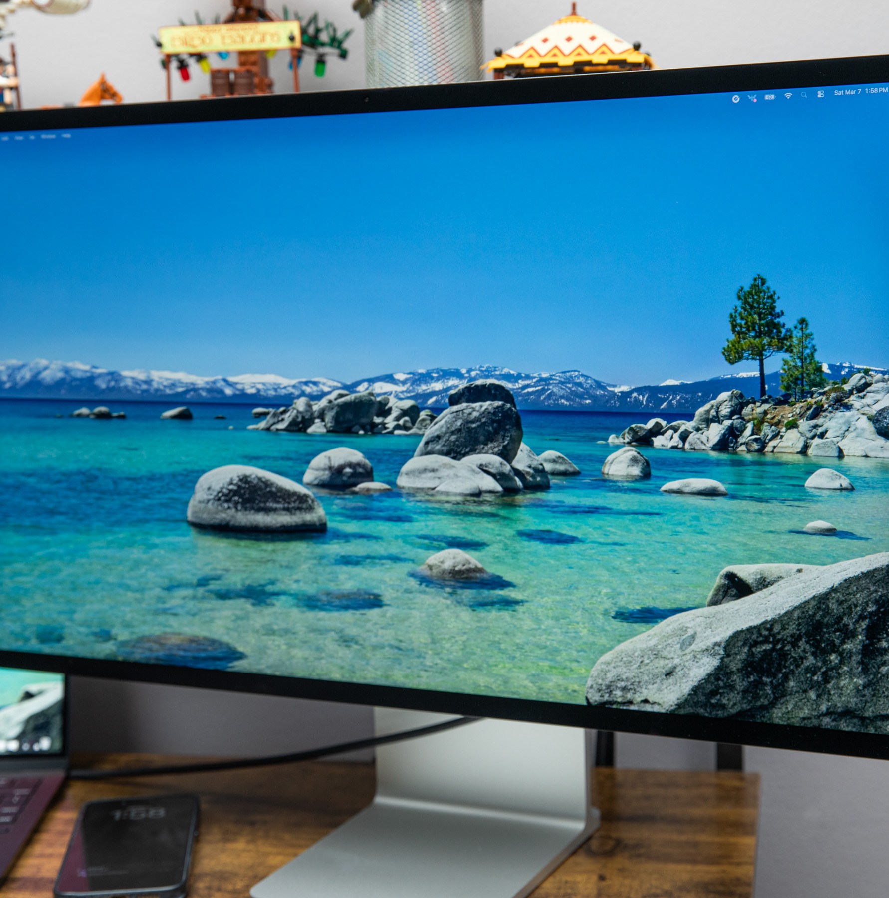 The Apple Studio Display XDR displaying a water landscape on a wooden desk next to a Macbook.