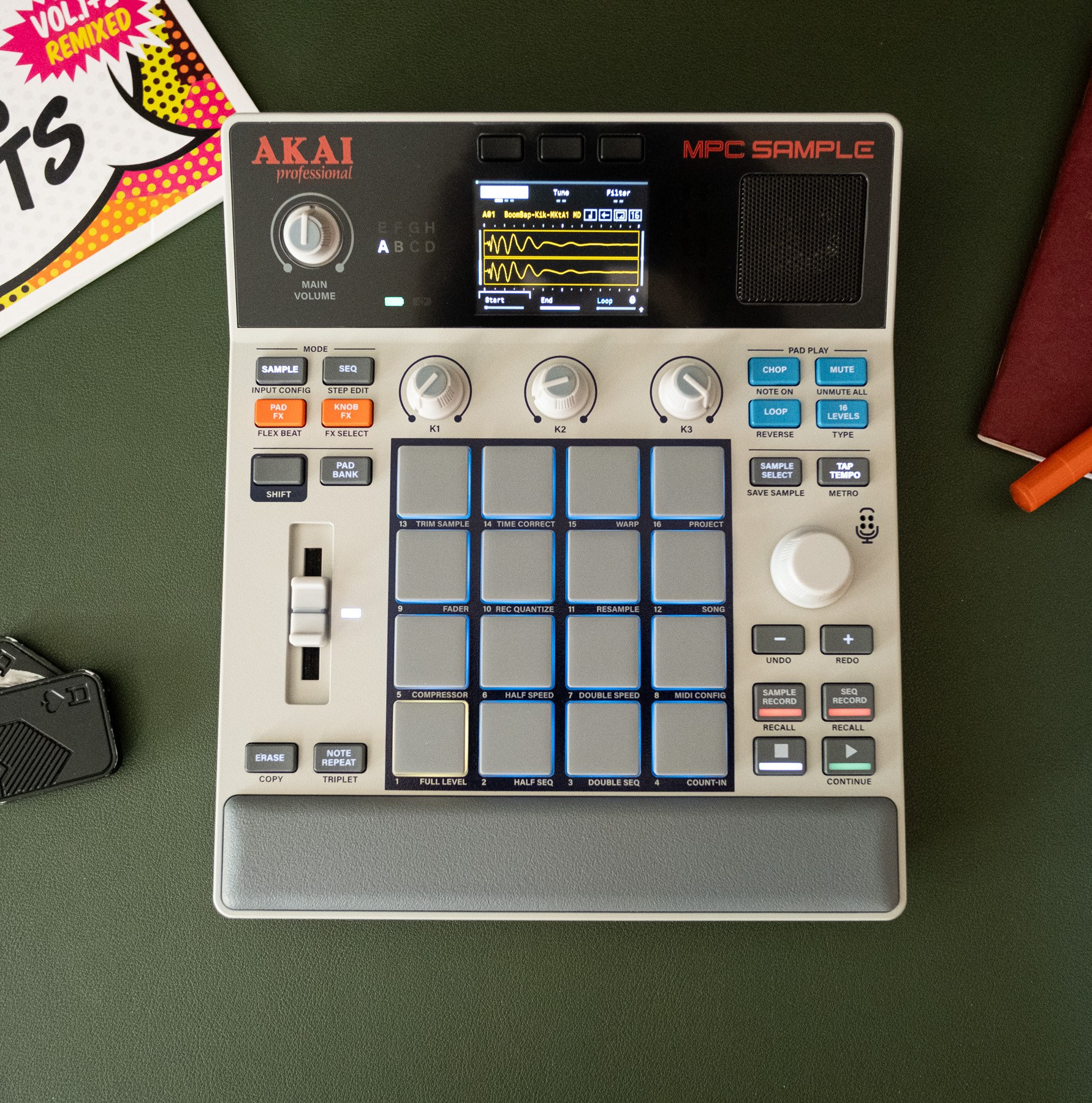 The MPC Sample on a desk with a scratch vinyl, fidget toy, pen, and a very pretty Field Notes notebook.