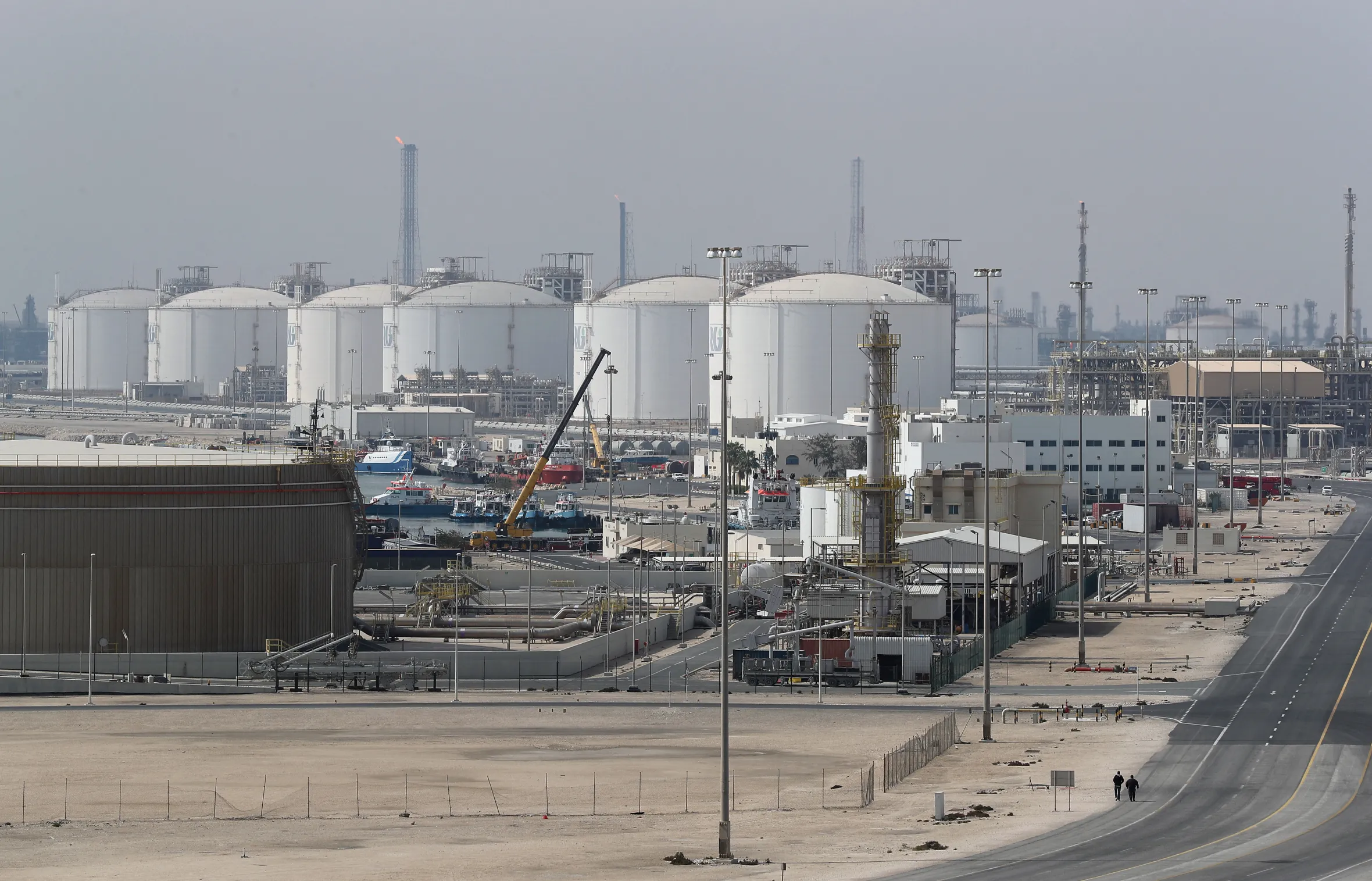 Ras Laffan Industrial City, Qatar, with large white natural gas storage tanks and port facilities.