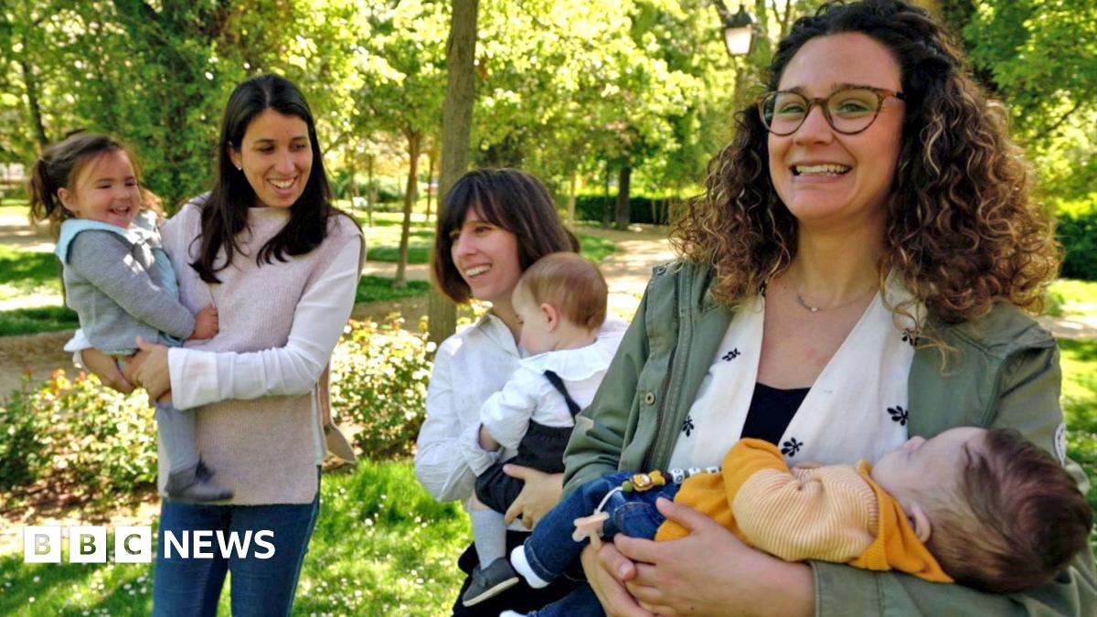 Tania has brown hair and is holding her baby in a sunny park.