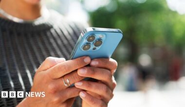 A close up of a person's hands holding a blue iphone, which we can only see the back of.