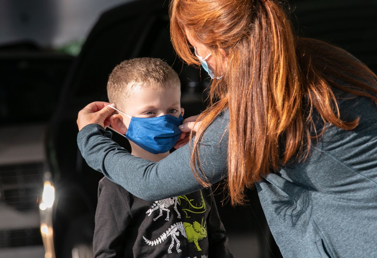 Teacher putting a mask on a school pupil during the pandemic (stock)