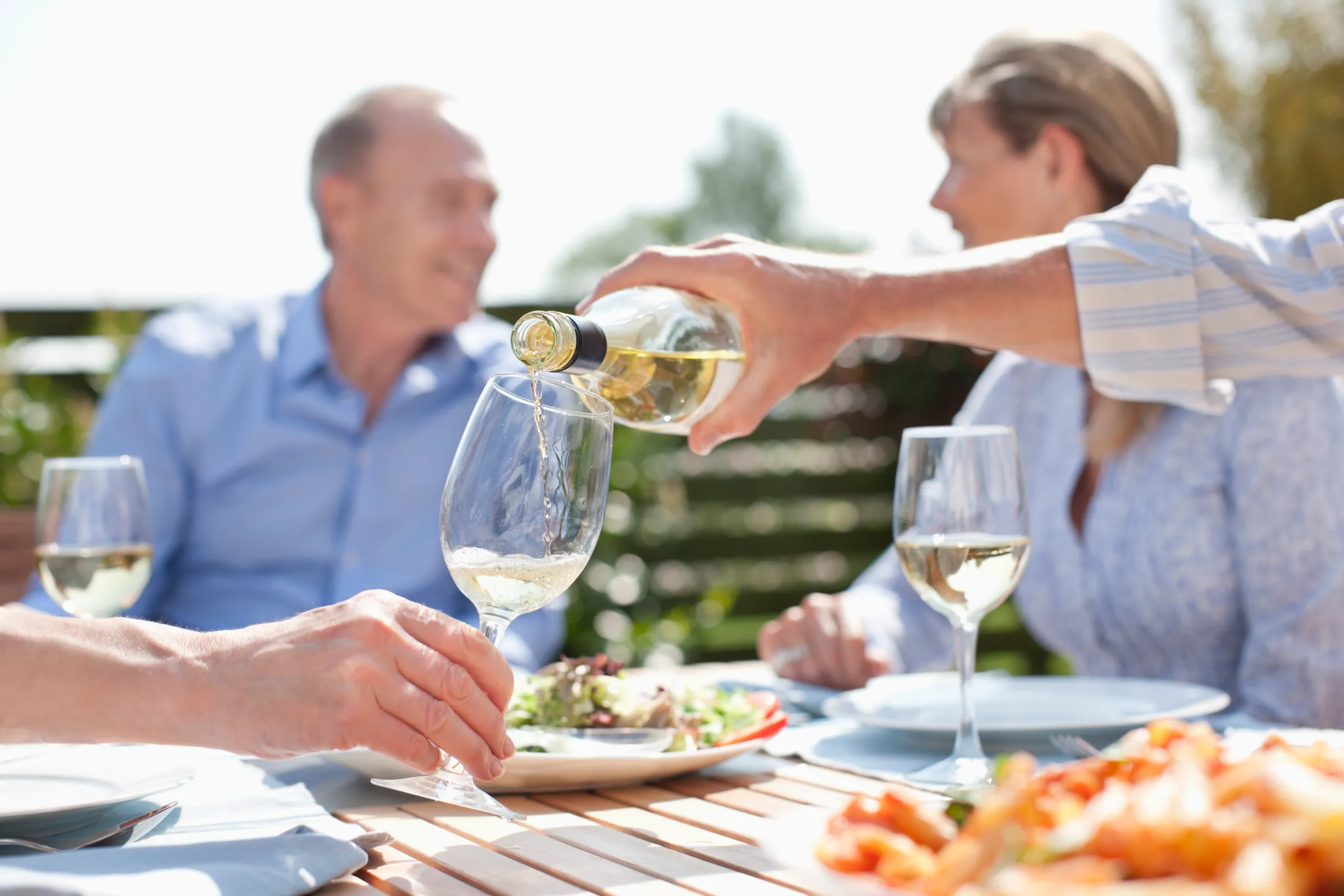 A man pouring white wine into a glass held by another person at an outdoor table.
