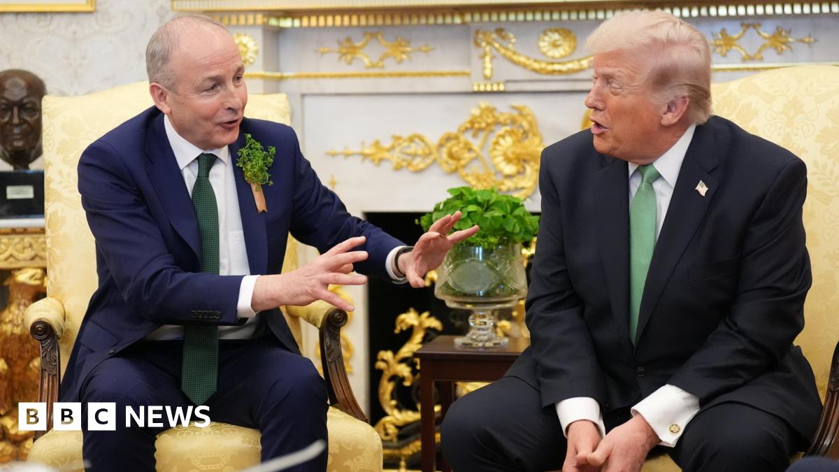 Martin and Trump are sitting next to each other in a room with a fire place, a bust of a head and a glass vase. Martin's hands are up as he talks.