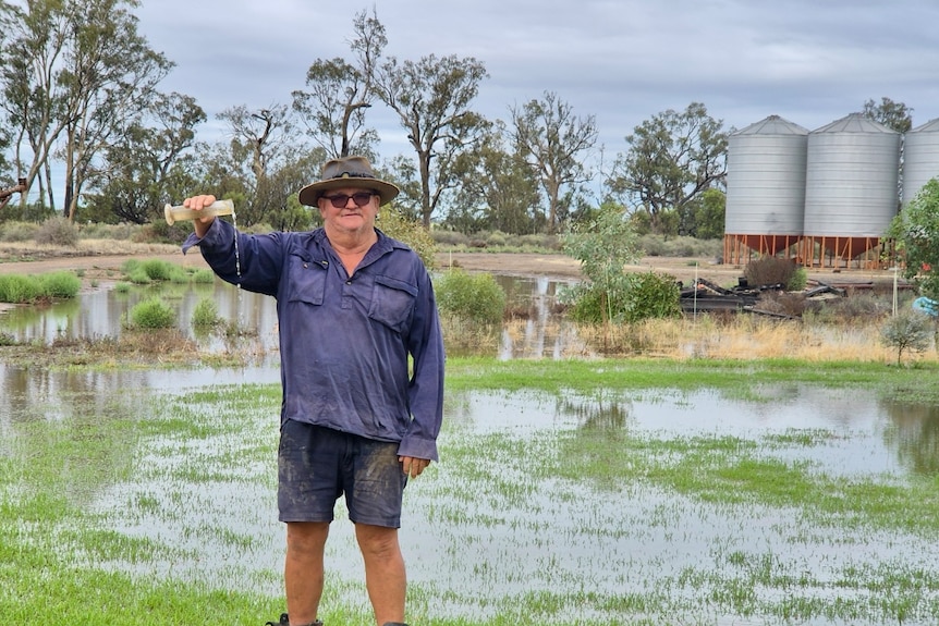 A man in a big hat tips rain out of guage standing on flooded grass