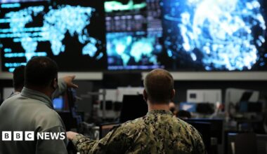 Two us cyber command officers in front of giant screens with data and information on them