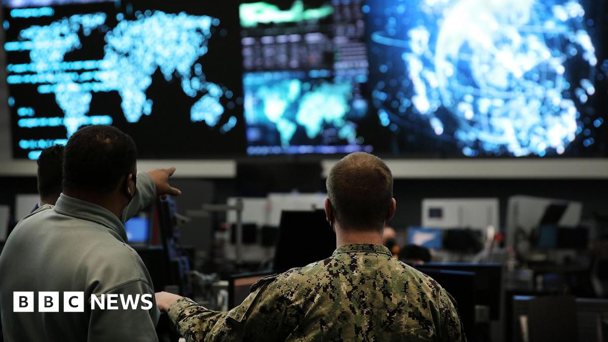 Two us cyber command officers in front of giant screens with data and information on them