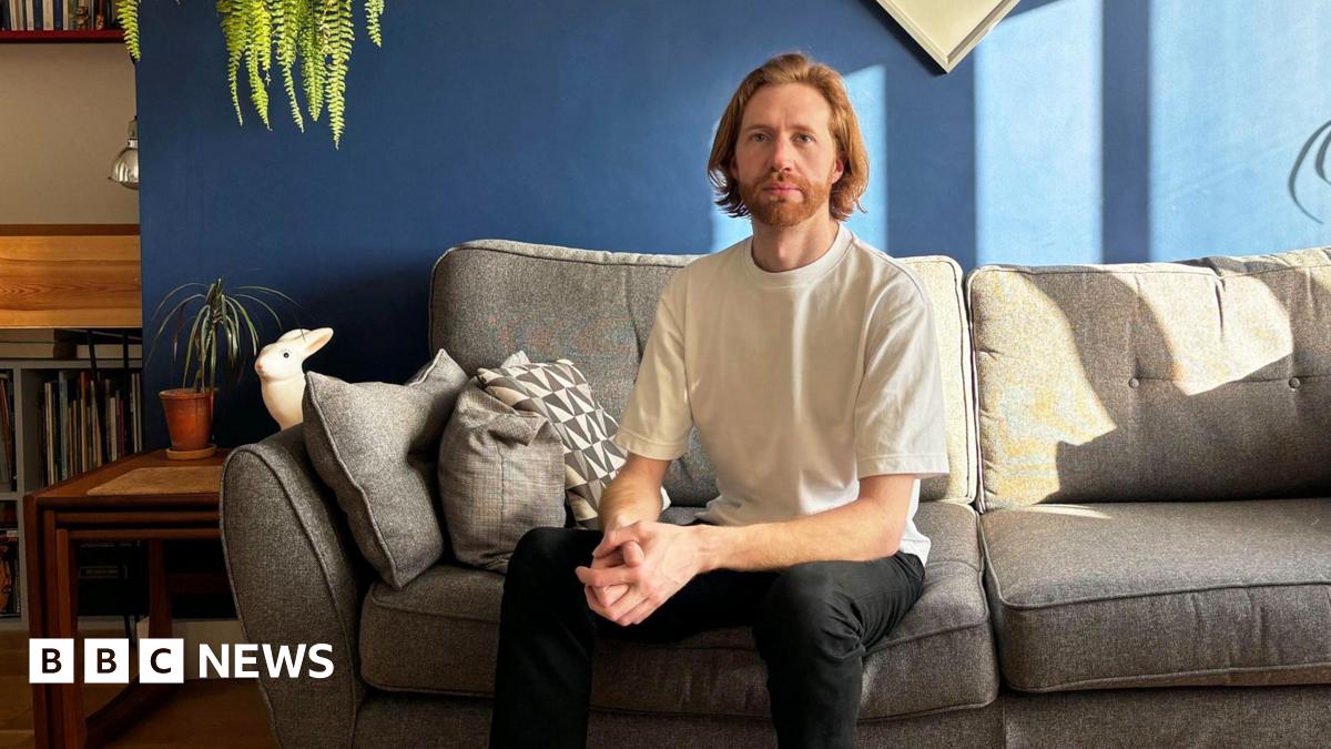 Male sitting on sofa wearing T shirt and dark trousers