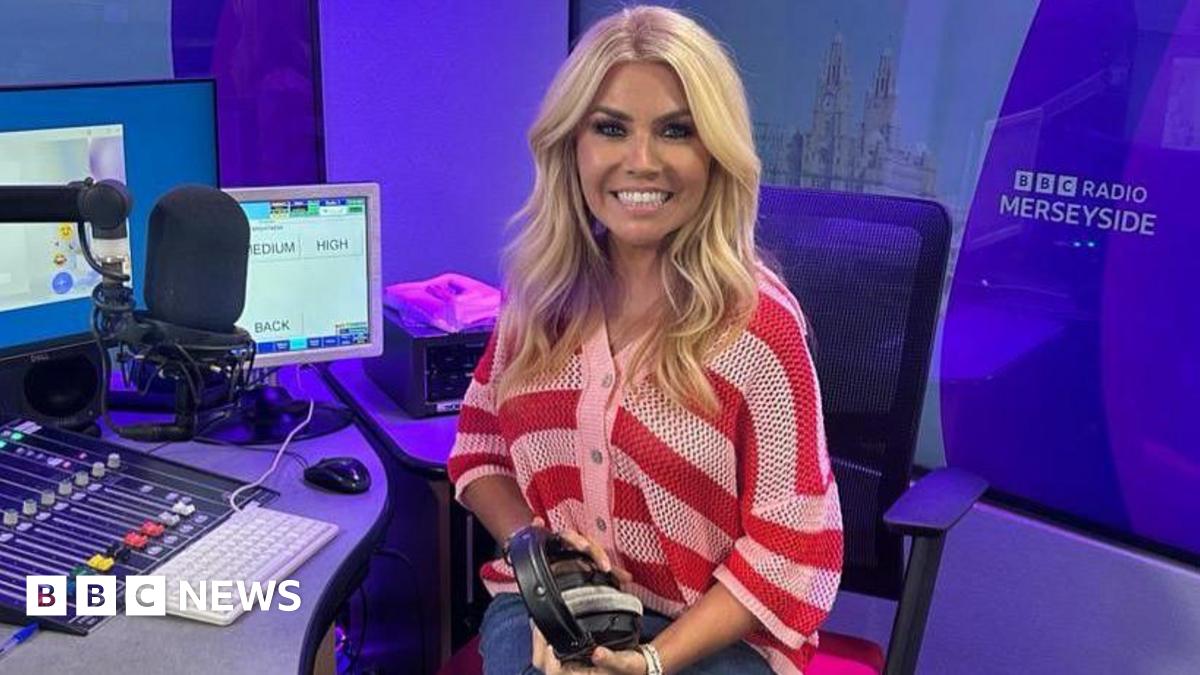 Leanne Campbell, who has wavy blonde hair and is wearing a chunky knit red and white striped cardigan, sits in a swivel chair by a studio desk with a large presenter's microphone to her right. She is holding a pair of black earphones.