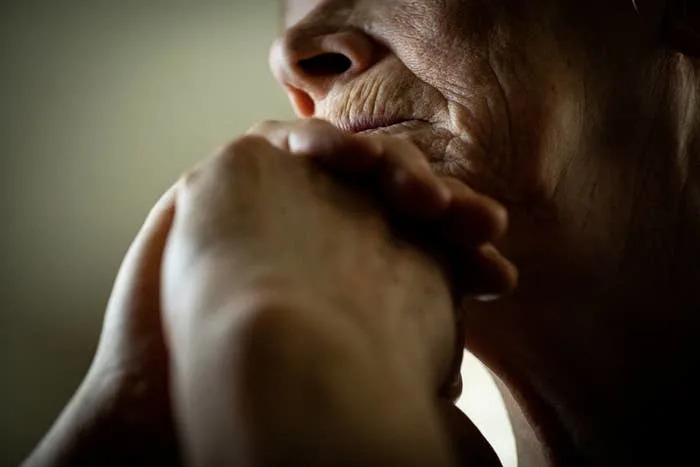 Close-up of an elderly person's contemplative expression, with hands clasped near their chin